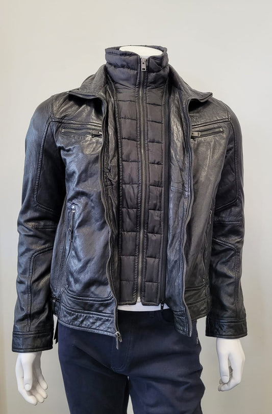 A mannequin wearing the Bain UF Men’s Leather Jacket by MAURITIUS LEATHER, featuring a black quilted insert over a zip-up vest and dark pants, stands against a plain light-colored background.