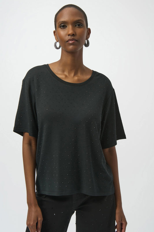 A person wears the Joseph Ribkoff Knit Scoop Neck T-Shirt with Rhinestones 254968, loose-fitting and black, paired with straight black pants, standing against a plain white background.