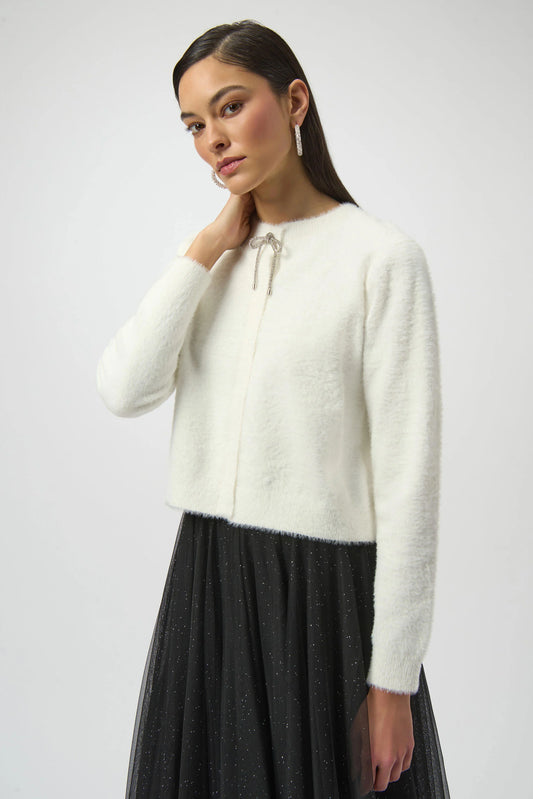 A woman with straight dark hair models the Joseph Ribkoff Feather Yarn Cardigan with Rhinestone Bow 254955 against a plain light background, gazing softly at the camera.
