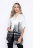 A woman with long, wavy blonde hair wears the Picadilly Oversized Shirt GM262XK, made from lightweight fabric with a black and white abstract print. She stands against a plain white background, one hand in her pocket.