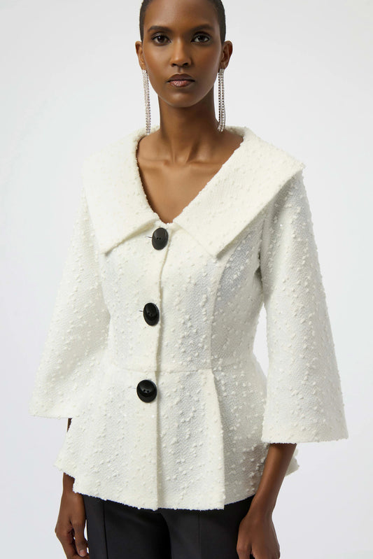A person wears the Joseph Ribkoff Sequined Bouclé Knit Peplum Jacket 254184—textured white with large black buttons, wide collar, and three-quarter bell sleeves—paired with dark pants against a plain background.
