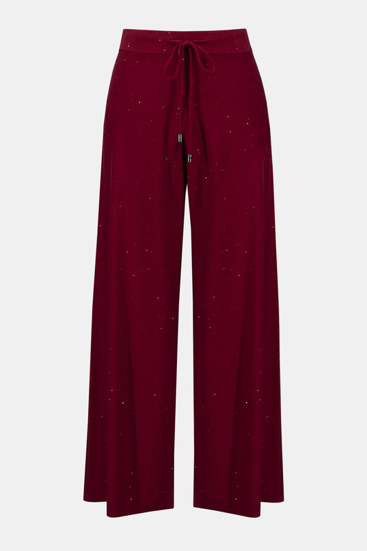 Joseph Ribkoff Sequined Sweater Knit Culotte Pants 244922F25 feature a wide-leg silhouette, elastic waistband with drawstring, and subtle sparkly speckles throughout the maroon sequin sweater knit fabric.