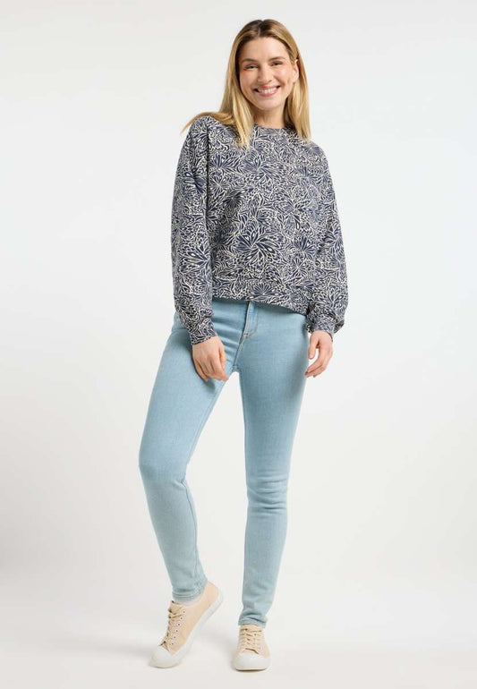 A person smiles against a plain backdrop, wearing RAGWEAR's WUSS PRINT SWEATSHIRT 2511-30006-2000 with light blue jeans and light-colored sneakers, their hands resting casually at their sides for a relaxed fit.