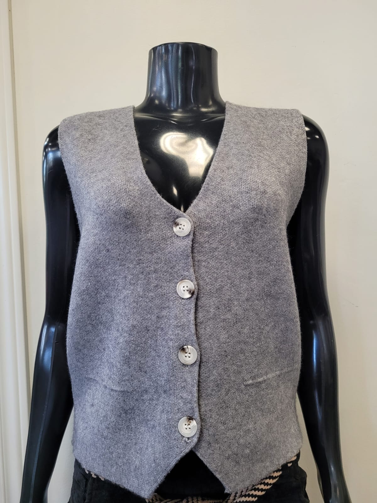 The ETERNELLE Button Up Knit Vest -eternelle is a sleeveless, light grey knit vest with four white front buttons, shown on a black mannequin against a plain background—a classic addition to any wardrobe.