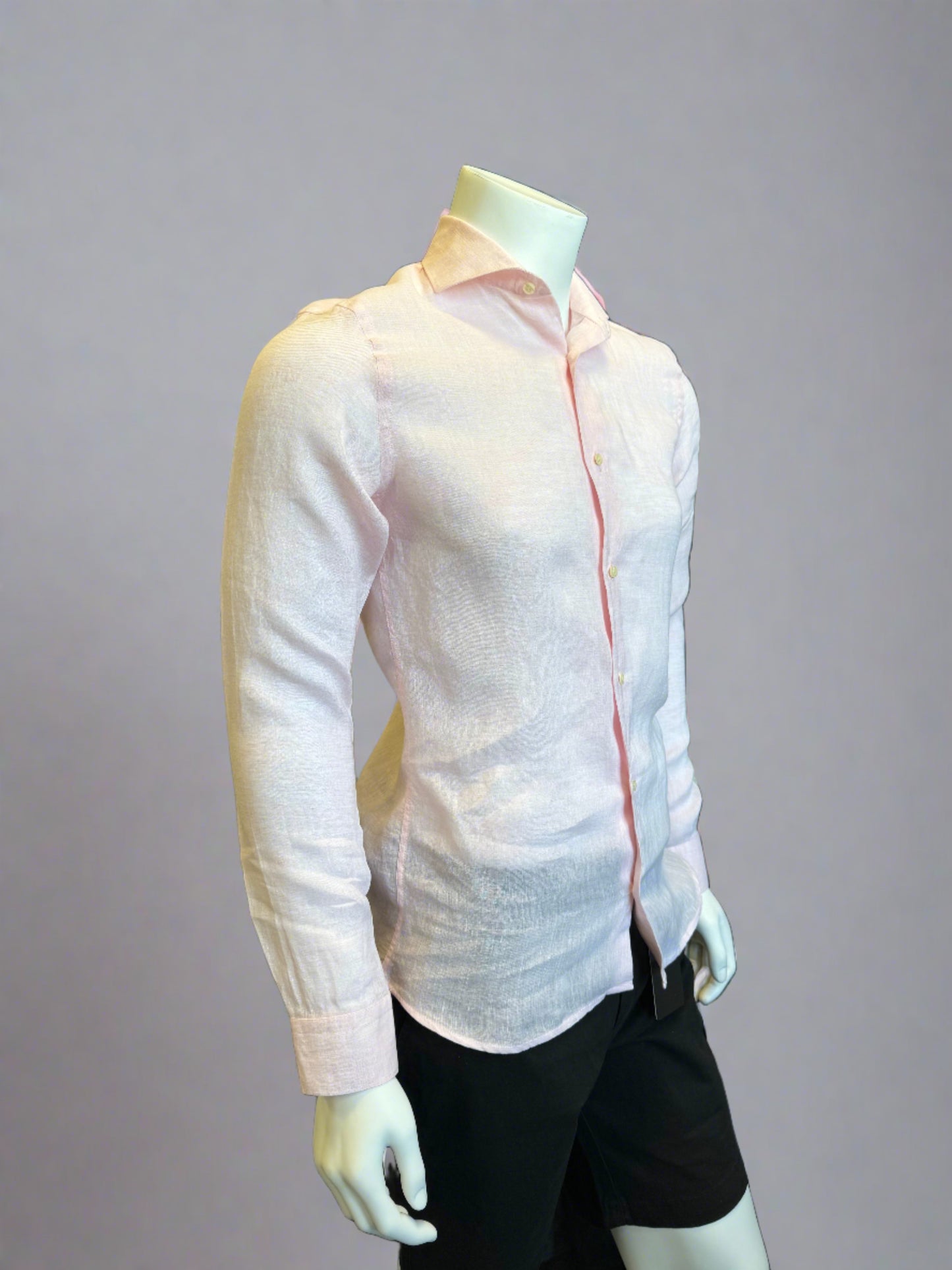 A mannequin is dressed in a slightly sheer, light pink Paul Miranda Linen Shirt Rosa paired with black pants. The 100% linen shirt by Paul Miranda, made in Italy, is fitted, highlighting the shape of the torso. The background is a plain grey shade.