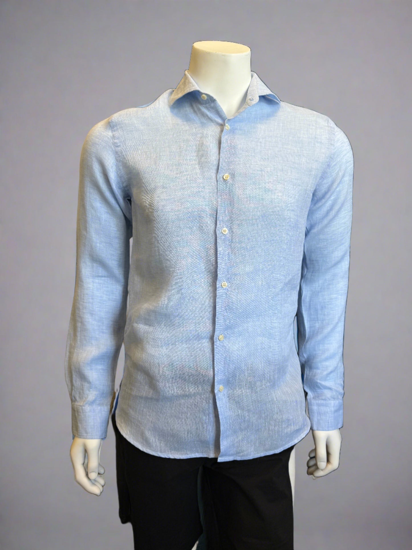 A headless mannequin showcases a Paul Miranda Linen Shirt Cielo in light blue. Crafted in Italy from 100% linen, the slim-fit shirt is adorned with front buttons and buttoned cuffs. The mannequin, also sporting black pants, stands against a plain gray background, highlighting the shirt as the main focus.