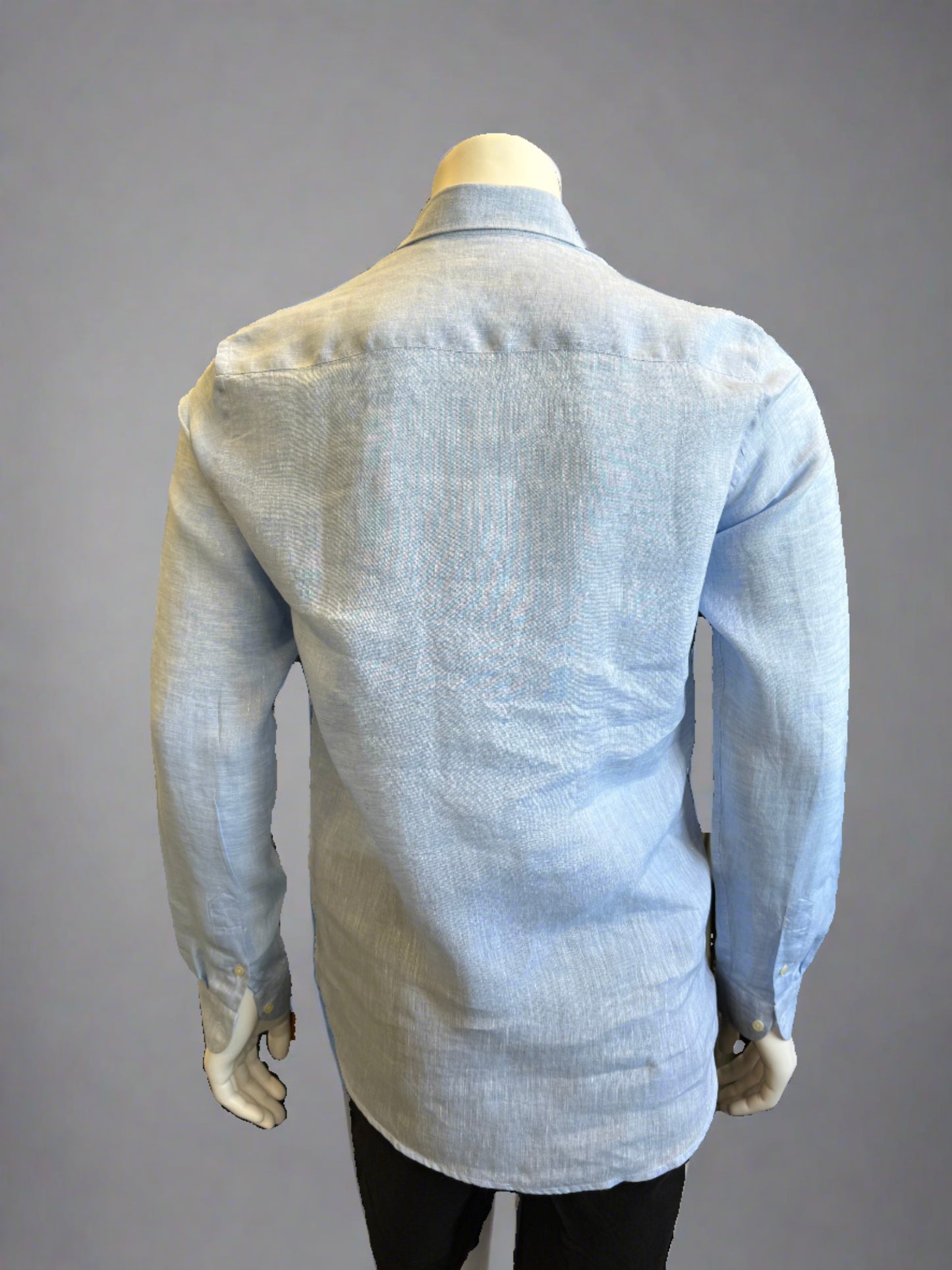 A headless mannequin showcases a Paul Miranda Linen Shirt Cielo in light blue. Crafted in Italy from 100% linen, the slim-fit shirt is adorned with front buttons and buttoned cuffs. The mannequin, also sporting black pants, stands against a plain gray background, highlighting the shirt as the main focus.