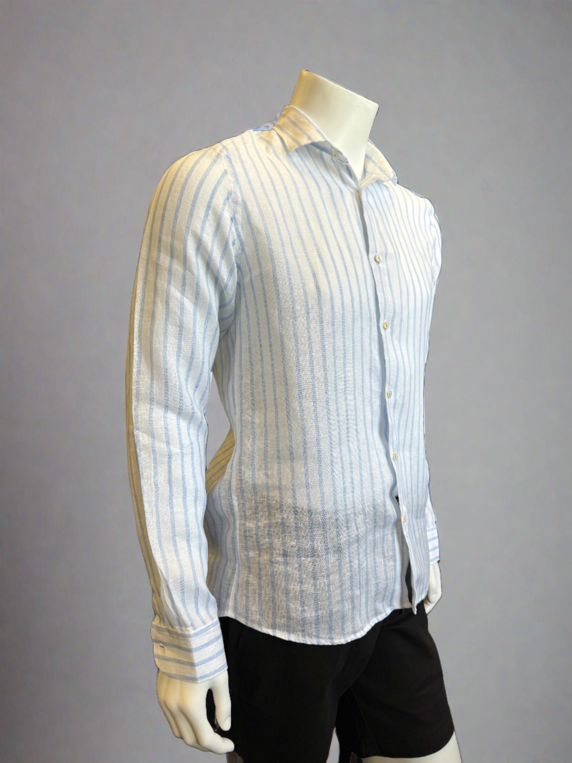 A mannequin dressed in a Paul Miranda Linen Shirt Striped Cielo, made from 100% linen and featuring vertical blue and white stripes. This long-sleeved, button-up shirt with a collar is crafted in Italy and paired with black pants. The background is a plain light grey.