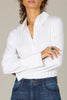 A woman in the Wit & Wisdom LONG FRENCH CUFF SLEEVE BUTTON DOWN PETITE WOVEN TOP and blue jeans stands with her arms crossed. She has curly hair, gold hoop earrings, a gold necklace, and a dark statement ring. Her face is partially visible.