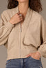 A woman with curly hair models the Wit & Wisdom LONG DOLMAN SLEEVE V-NECK ZIP FRONT SWEATER JACKET in beige, styled with blue jeans, rings, and a bracelet—showcasing chic modern fashion.