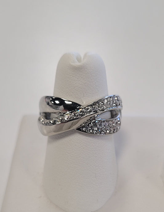 The Jenna-70 Adjustable Ring by Elise Accessories features double twisted bands—one with sparkling CZ stones and one smoothly polished—presented on a white ring holder, ideal for anyone who loves elegant jewelry.