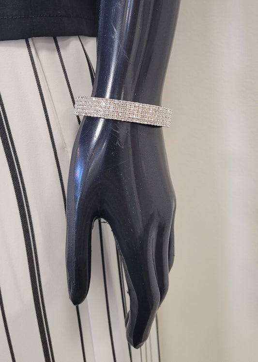 A mannequin hand displays the Mimosa 19 Bracelet by Elise accessories, its rhinestones sparkling against a black and white vertically striped skirt.