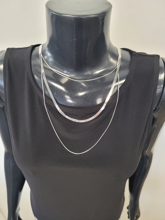 A black mannequin showcases the sleeveless black top, adorned with two layered Rhea-21 silver necklaces by Elise Accessories. The plain, light backdrop emphasizes this elegant, chic style.