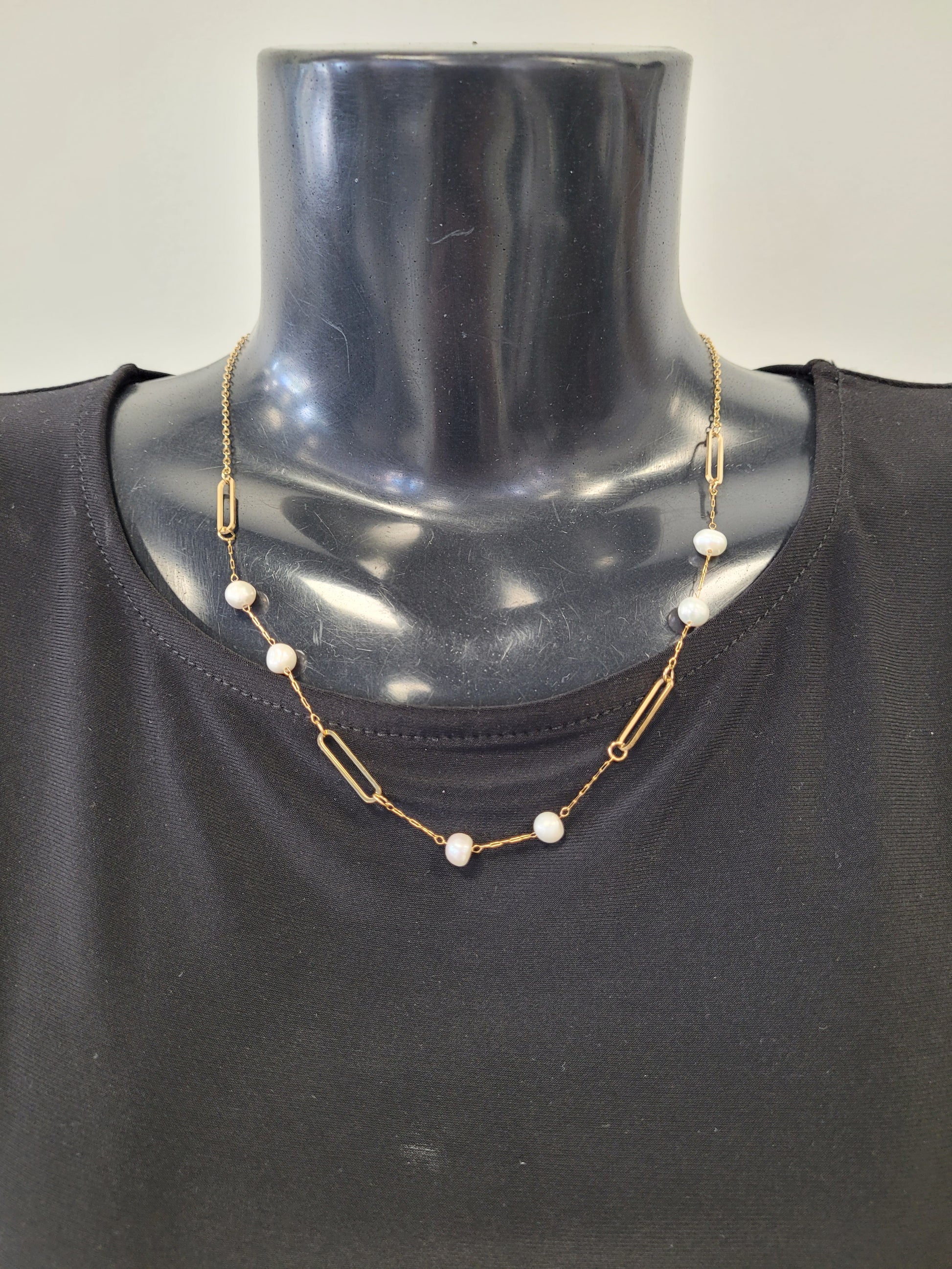 The Elena-4 Necklace by Elise accessories is a gold paperclip link chain with alternating pearls, shown on a black mannequin bust in a black top for a chic, modern look.