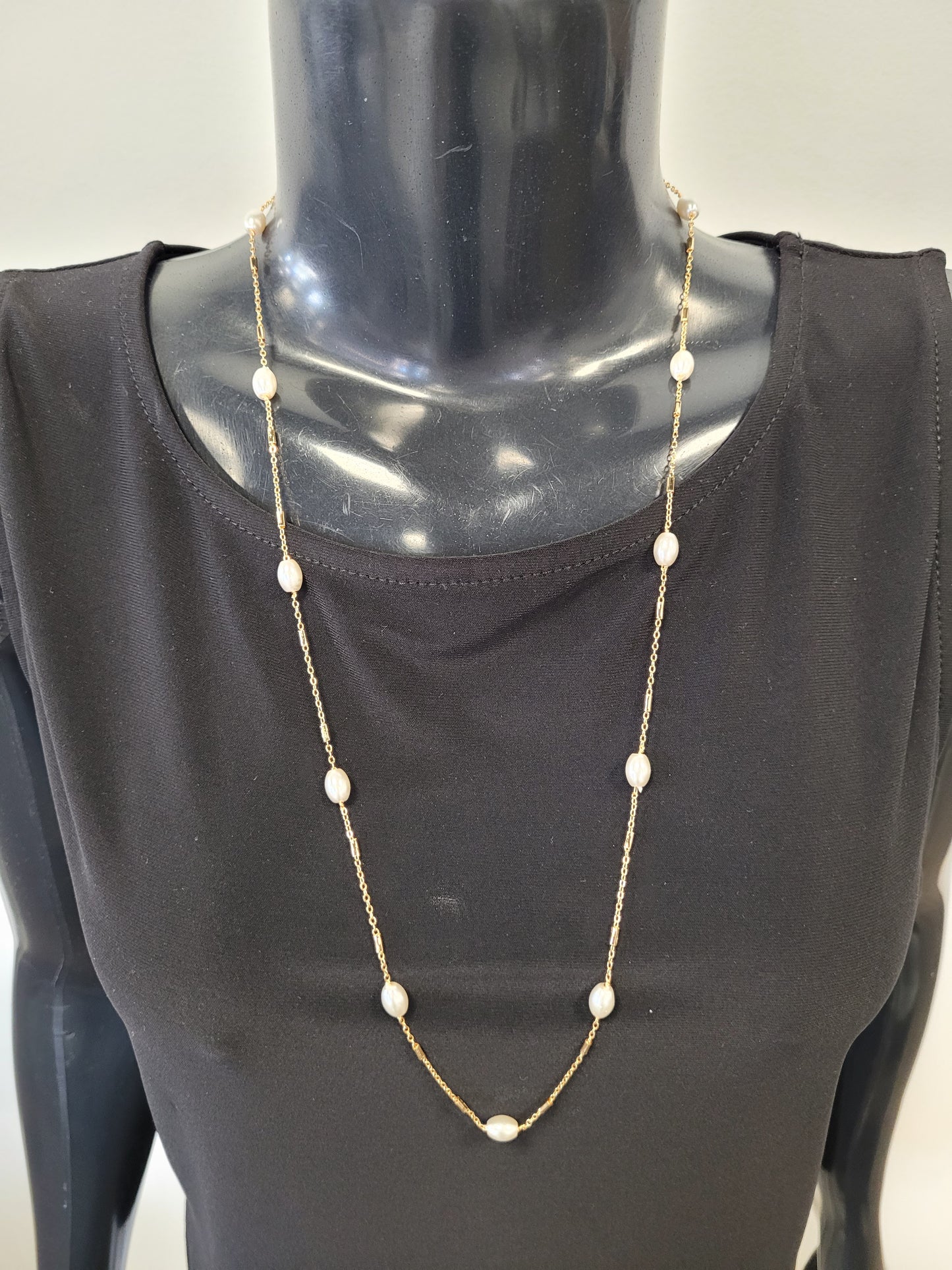 A mannequin in a black top showcases the Fiona-25 Necklace by Elise accessories, a timeless piece featuring stationed pearls along a long gold chain.