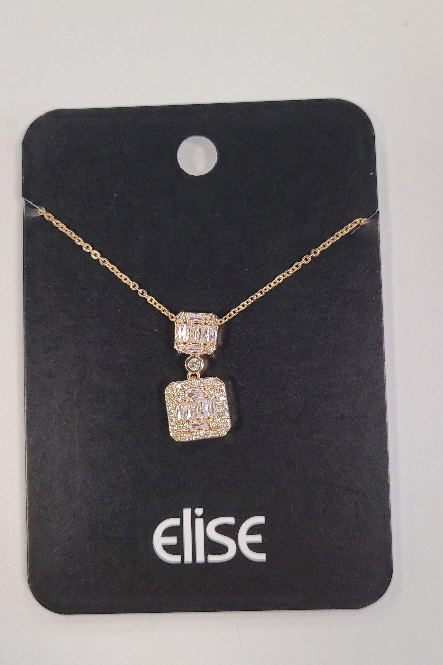 The Trina-2 Necklace from Elise accessories features an elegant gold chain with two CZ square diamond-studded pendants, displayed neatly on a black "elise" card—an ideal piece for any jewelry collection.