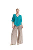A person wearing the TINY GLACIER TOP by Oh My Gauze, beige wide-leg pants, yellow earrings, and green sandals poses against a plain white background.