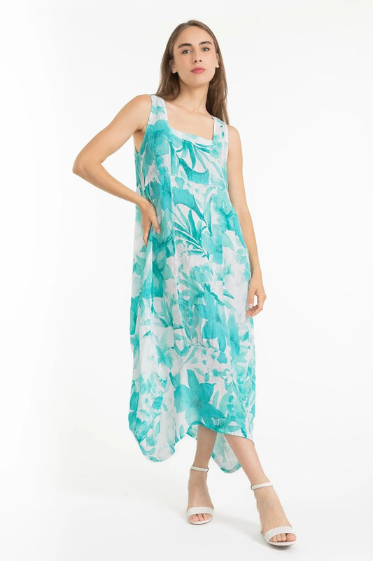 A woman models the French Linen Dress TP1612-11 Bianco from LinenLuv, its eco-friendly linen in a teal and white abstract pattern. In a white studio, she stands poised with one hand on her hip, her style enhanced by chic white strappy heels.