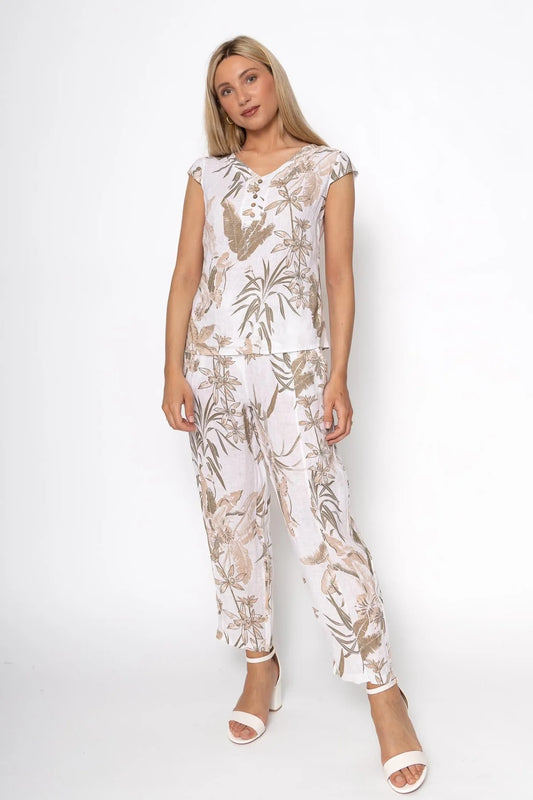 Against a plain backdrop, an individual wears LinenLuv's eco-friendly French Linen Top (TP1492-11 Bianco) paired with matching wide-leg pants in muted brown and pink florals. White open-toe sandals complete the sustainable look.