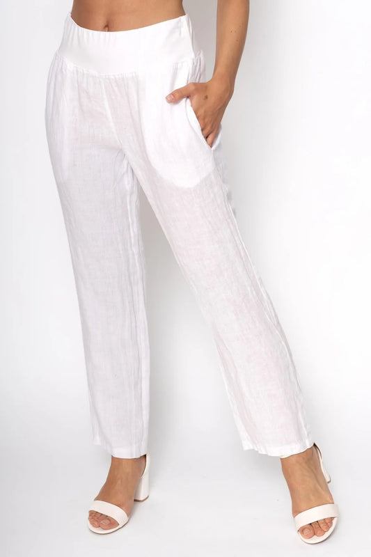 A person wears loose-fitting, eco-friendly French Linen Pant PT830-11 Bianco by LinenLuv, with hands in pockets and white open-toed sandals, against a plain white backdrop.