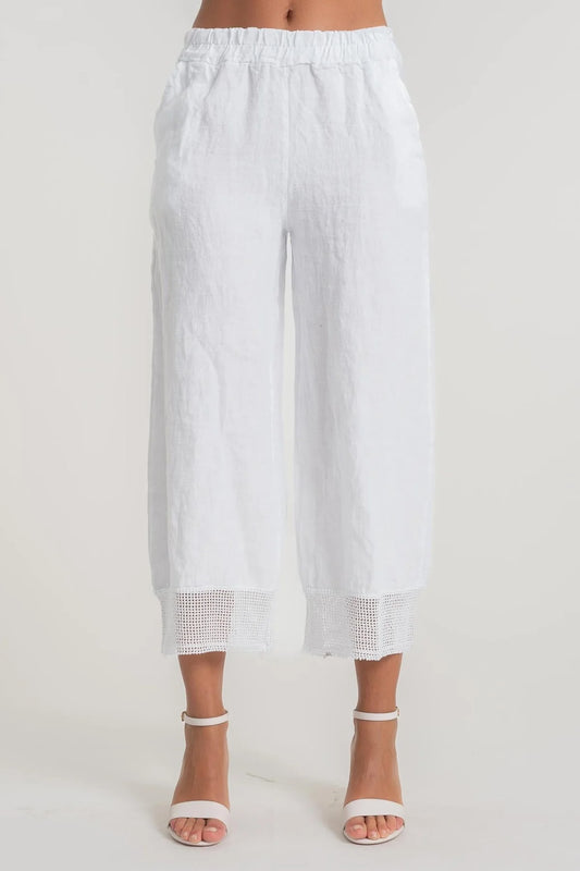 A person wearing LinenLuv's French Linen Pant PT840-11 Bianco, showcasing eco-friendly white linen with crochet cuff details, stands against a neutral background. The pants feature an elastic waistband and are paired with white open-toed heels.