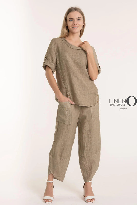 A person smiles in a matching beige set, wearing a French Linen Blouse TP1340-148 Natural by LinenO. The outfit contains a 100% European linen short-sleeve top with rolled sleeves and loose pants, against a plain white backdrop with the LinenO logo on the right.
