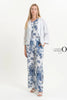A woman stands against a plain background, wearing an eco-friendly white linen outfit with blue floral patterns. Her ensemble features the French Linen Jacket TP1523-11 Bianco by LinenO, paired with matching top and pants. White sandals complete the look, while "LinenO" appears nearby.