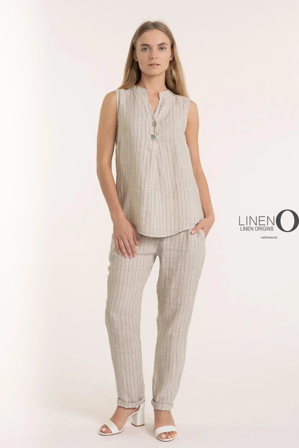 A person wears the French Linen Top TP1495-9 Beige from LinenO, a sleeveless pinstriped top made from 100% European linen, paired with matching pants. White heeled sandals complete the eco-friendly look, set against a light background with "Linen Origins" displayed on the right.