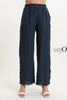 A person wears the stylish French Linen Pant PT839-75 Notte by LinenO, featuring wide-leg dark blue European linen with frayed hem and wooden buttons near the bottom. Paired with white open-toed heels on a crisp white background, it highlights eco-friendly fashion choices.