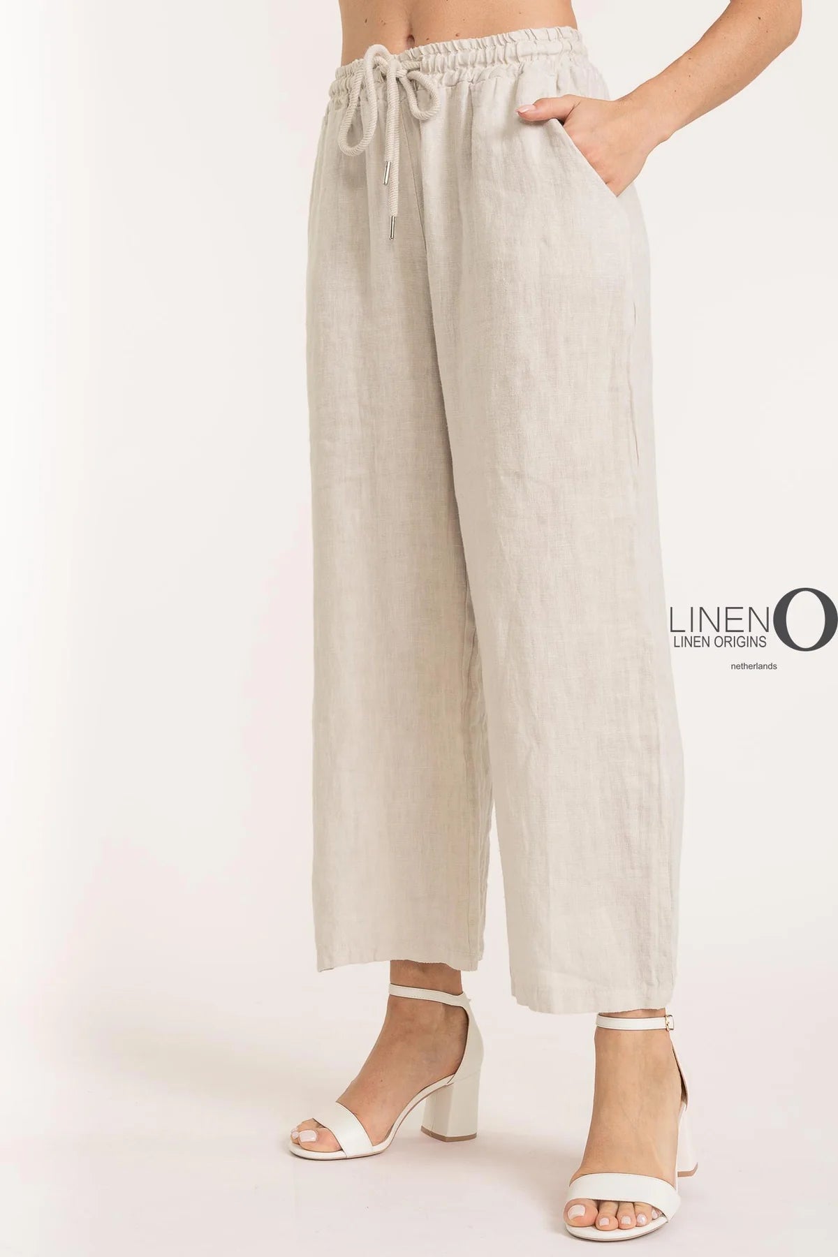 A person in LinenO's French Linen Pant PT837-9 Beige, featuring an elastic waistband and side pockets, is paired with white high-heeled sandals against a white backdrop.
