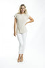 A woman with long blonde hair smiles against a white background, wearing the ORIENTIQUE Essentials Boatneck Knit Top (Style: 1276) in beige, paired with white pants and beige heeled sandals. One hand rests on her hip.