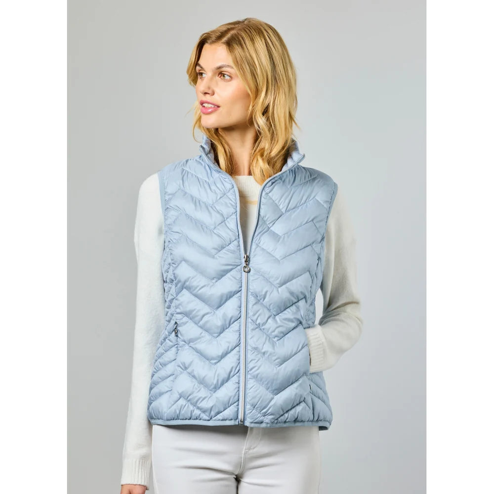 A woman wears the JUNGE Louise Vest in Lagoon (0126-4040-62) over a white long-sleeve sweater, standing with one hand in her pocket against a plain light background—ideal for transitional layering.