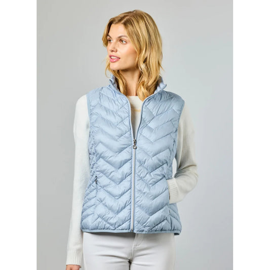 A woman wears the JUNGE Louise Vest in Lagoon (0126-4040-62) over a white long-sleeve sweater, standing with one hand in her pocket against a plain light background—ideal for transitional layering.