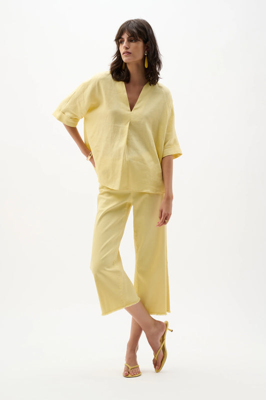 A woman poses against a white background wearing the Joseph Ribkoff Linen Straight Top With V-notch neckline in Mellow Yellow, paired with matching wide-legged cropped pants, yellow heeled sandals, and yellow earrings.
