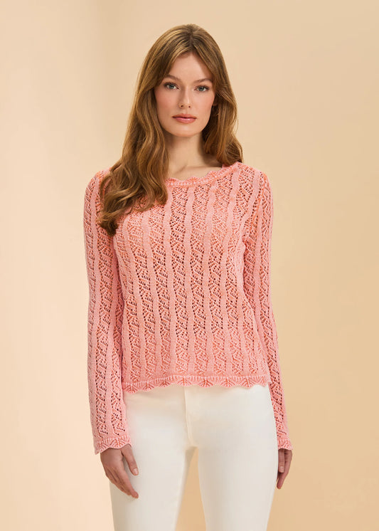 A woman with long, light brown hair models the French Dressing Jeans Long Sleeve Garment Dye Sweater in Cantaloupe, standing against a plain beige background and looking at the camera with a neutral expression.