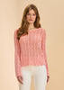 A woman with long, light brown hair models the French Dressing Jeans Long Sleeve Garment Dye Sweater in Cantaloupe, standing against a plain beige background and looking at the camera with a neutral expression.