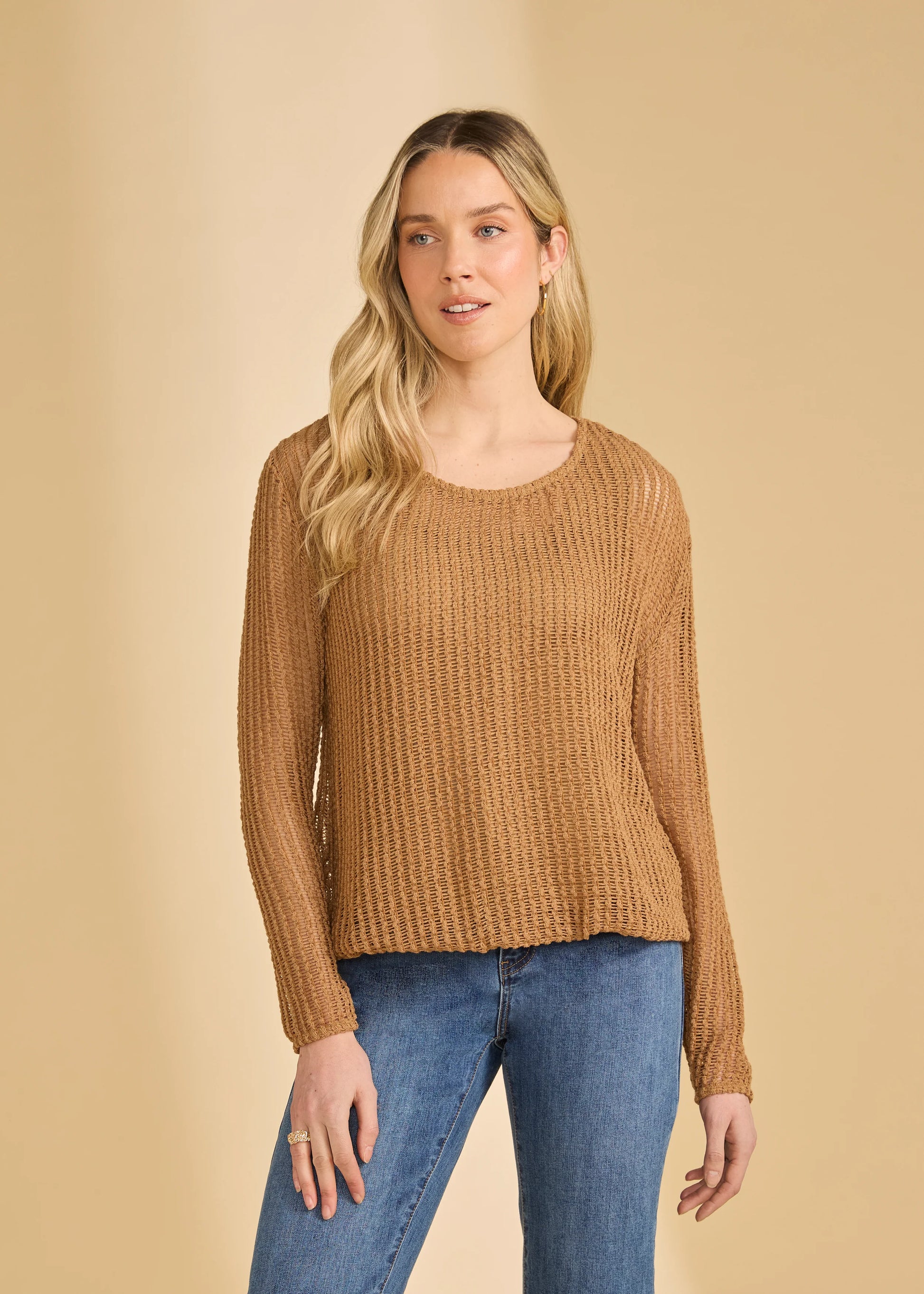 A woman with long blonde hair wears the French Dressing Jeans Long Sleeve Bubble Top in Henna and blue jeans, standing against a beige background.