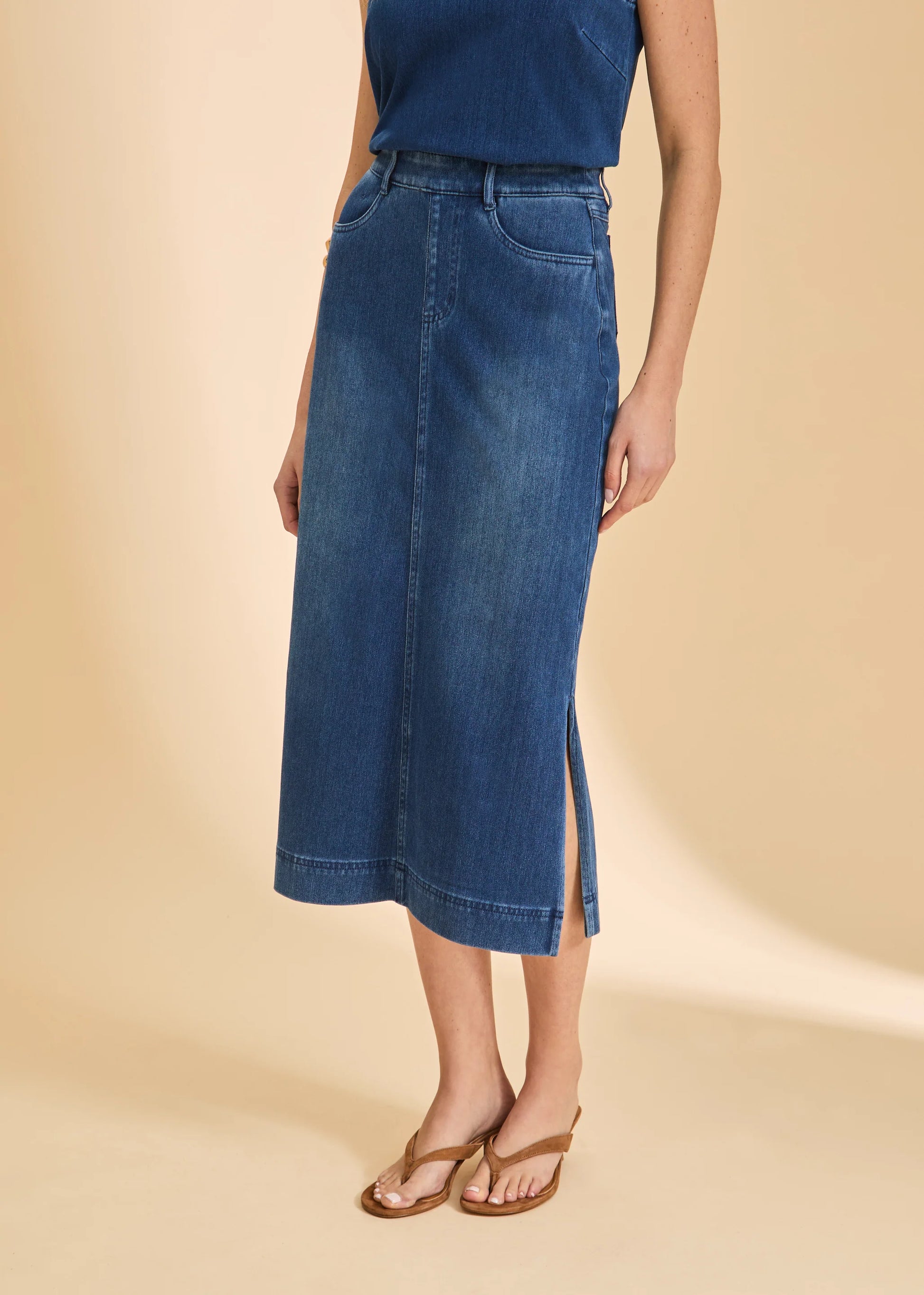 A person wears a blue sleeveless top, French Dressing Jeans Pull-On Skirt with Slits in Blue Denim (6983131-BLUDEM), and brown sandals, standing against a beige background.