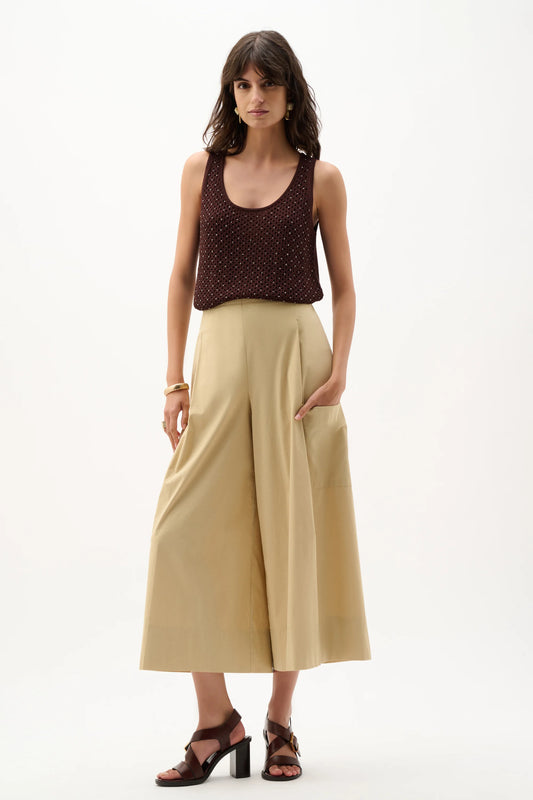 A woman stands against a plain white background wearing the Joseph Ribkoff Embellished Knit Camisole 262957, wide-leg beige high-waisted pants, brown heeled sandals, and a gold bracelet.