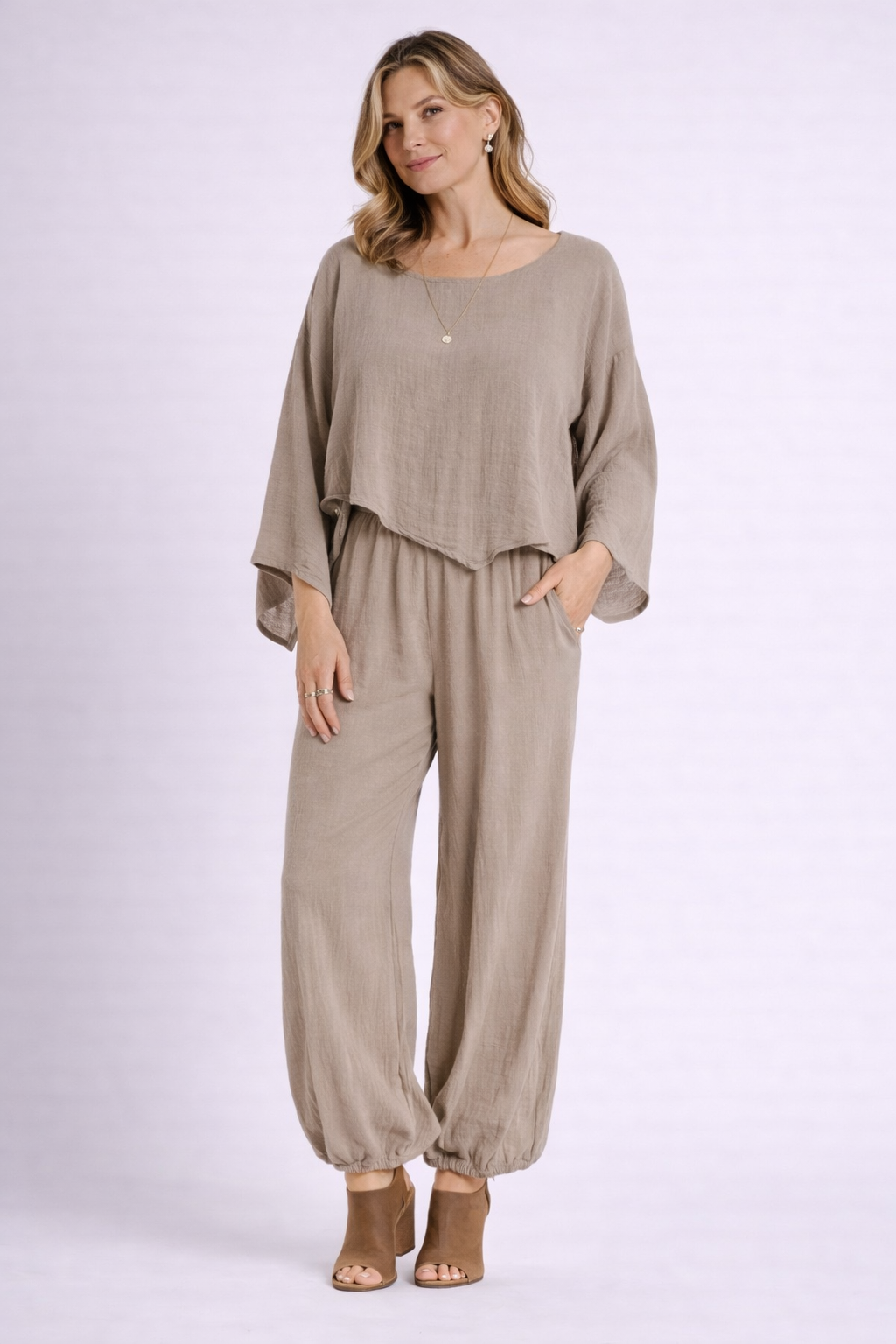 A woman wearing the Oh My Gauze Vanna Rye Blouse T668 and matching wide-leg pants with pockets, paired with tan open-toe heels, stands against a plain light background.