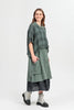 A woman in a BOXY LARGE CHECK SAGE GAUZE LINEN BLOUSE by Paolo Tricot, with a long skirt and light gray lace-up boots, stands smiling against a plain white background, looking to the side.