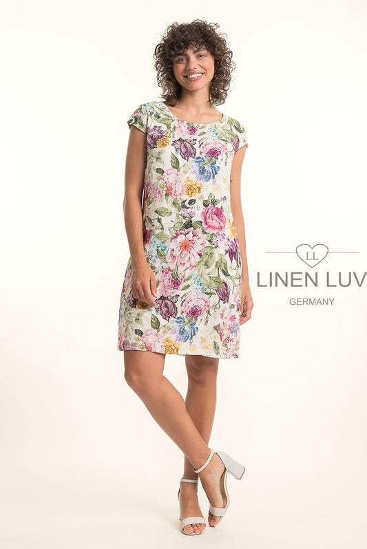 A woman smiles in a short-sleeved, knee-length French Linen Dress TP1764P-85 Pink by LinenLuv, featuring colorful floral prints. "LinenLuv" appears to the right against a light background.