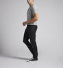 A person with cropped hair is standing and looking to the left in a gray short-sleeve t-shirt, Silver Jeans Co. Taavi Skinny Fit Skinny Leg Jeans in black eco wash made from max flex denim, and black low-top sneakers. The background is plain light gray.