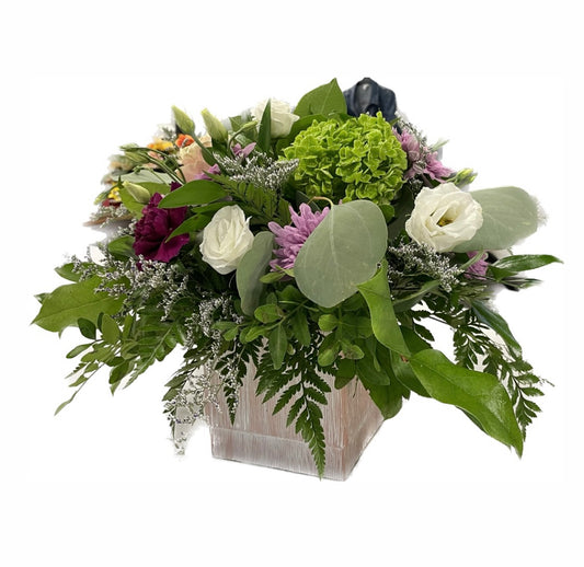 Introducing "Garden Moments" by Posies Flowers & Fashion: an exquisite floral arrangement in a white square vase, showcasing an assortment of greenery, light purple chrysanthemums, white roses, bright pink peonies, green hydrangeas, and small white filler flowers. With various shades of green foliage and textures, availability is limited.