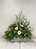 The "Elegant Sympathy" arrangement by Posies Flowers & Fashion showcases a serene touch with its rectangular design featuring white gerbera daisies, green hydrangeas, delicate dark red blooms, and sprigs of greenery, all beautifully arranged in a rustic wooden box. This modern funeral arrangement stands out gracefully against a plain backdrop.